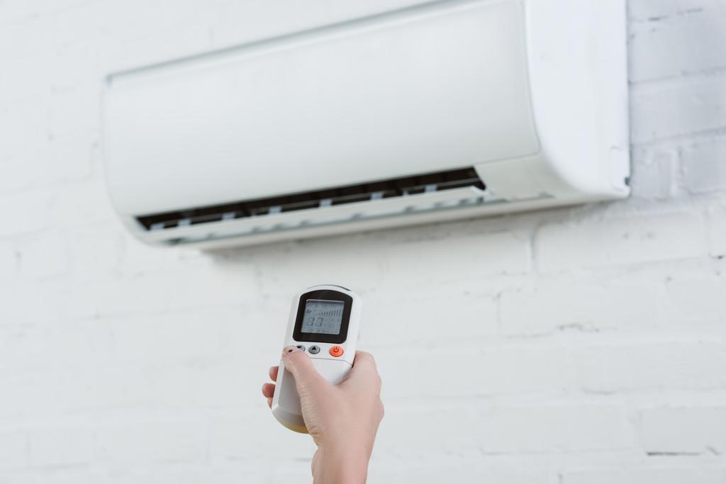 pointing at air conditioner hanging on white brick wall with remote control